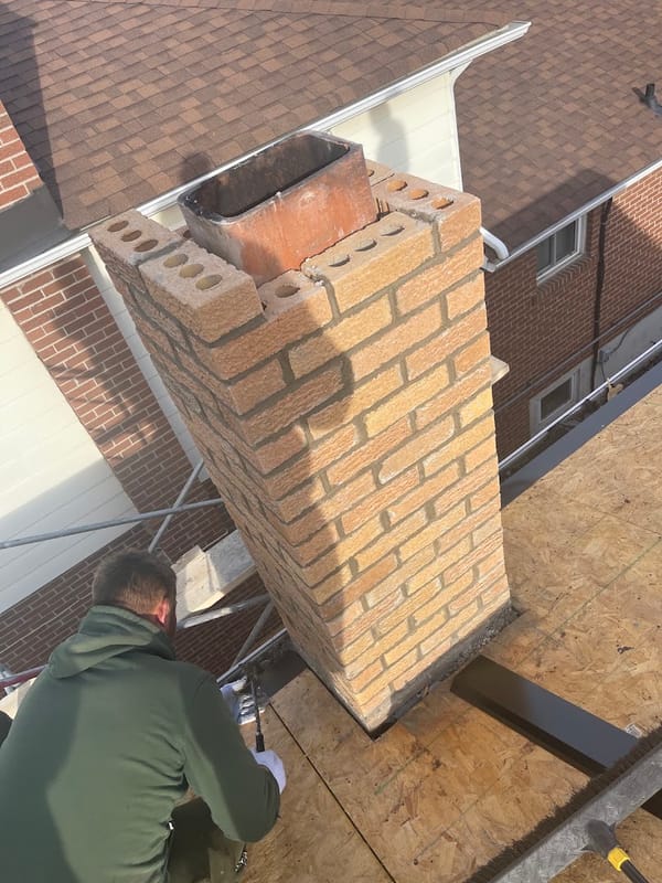 Roofer working beside a rebuilt buff-brick chimney on new roof decking